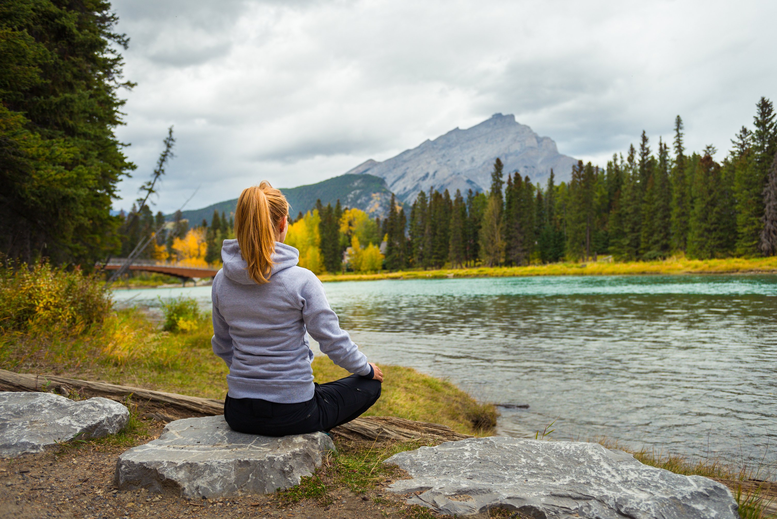 Woman Meditating by River in Autumn